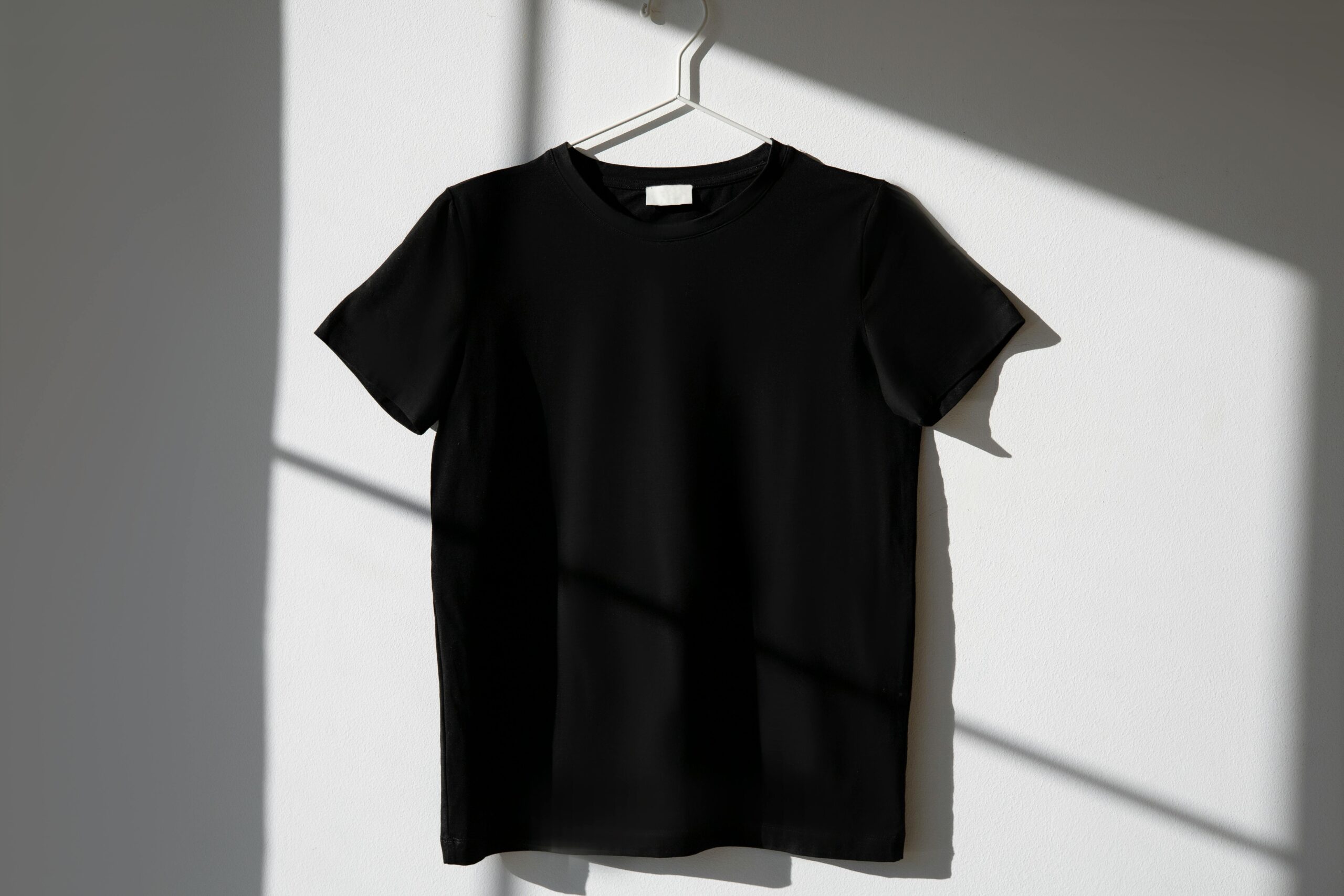 pexels photo 8532616 8532616 Minimalist image of a black t-shirt on a hanger with dramatic shadows on a white wall.
